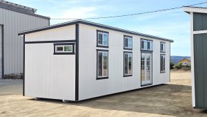 Two-story white modular building with black trim and multiple windows on a dirt construction site, Ply Gem windows visible in the panes.