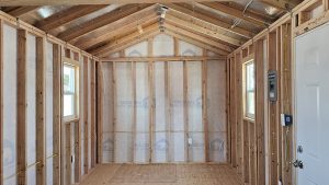 Unfinished room with exposed wooden studs, roof trusses, and electrical wiring visible throughout the framing.