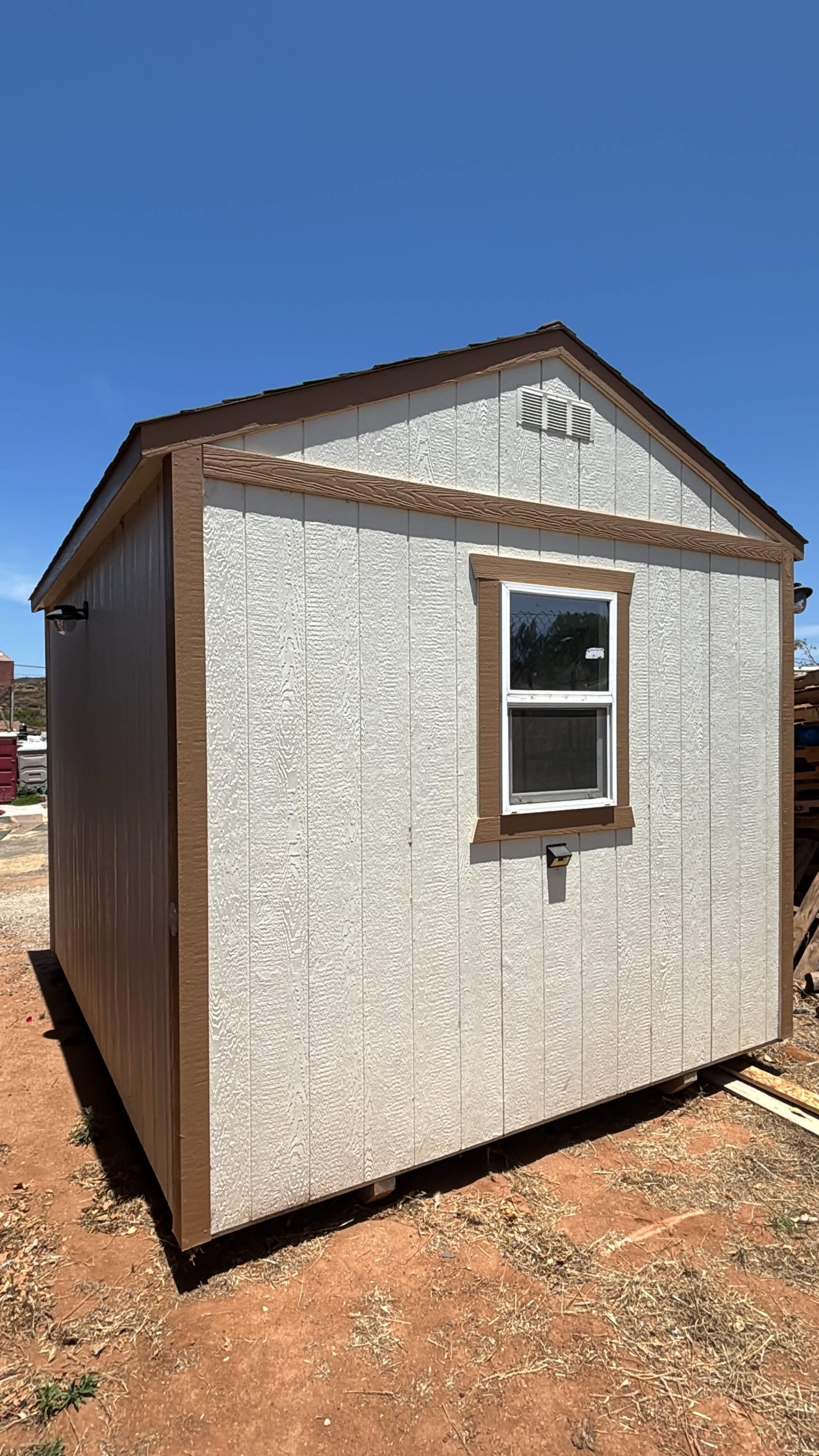 Small beige shed with brown trim and a single window under a clear blue sky.