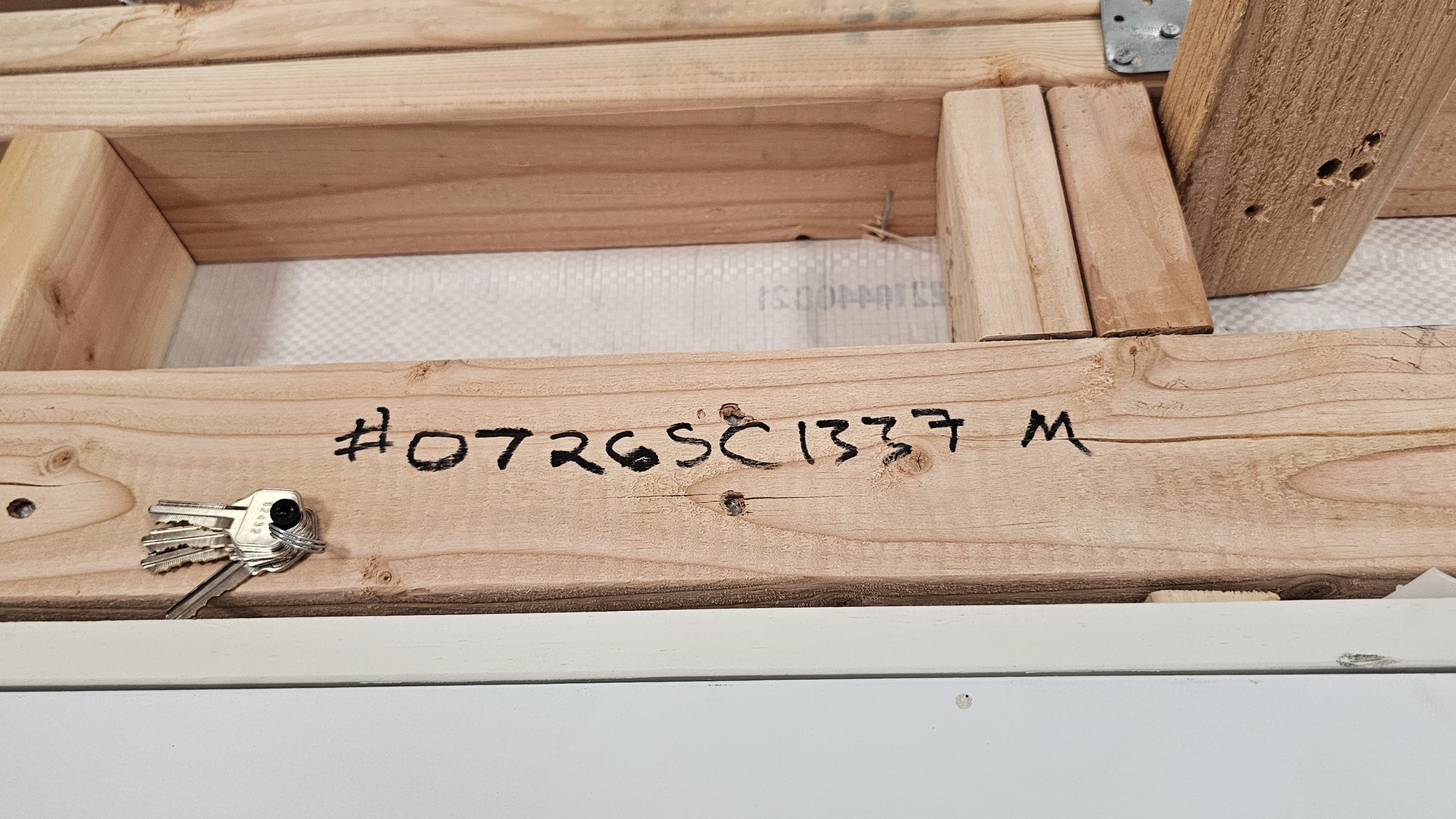 Wood framing with a small set of keys resting on a plywood beam; handwritten code '#0726SC1337 M' on the wood.