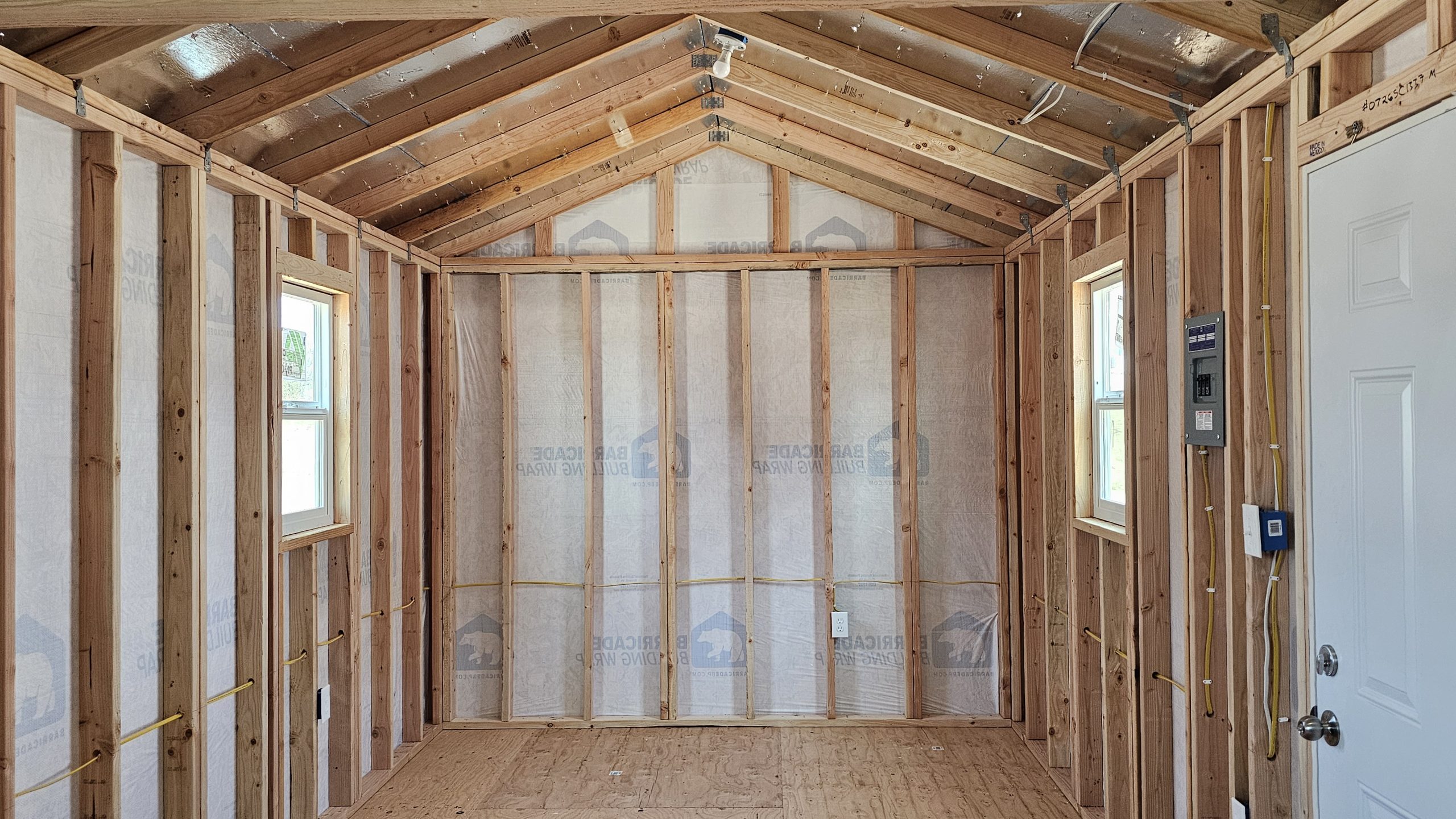 Unfinished room with exposed wooden studs, roof trusses, and electrical wiring visible throughout the framing.